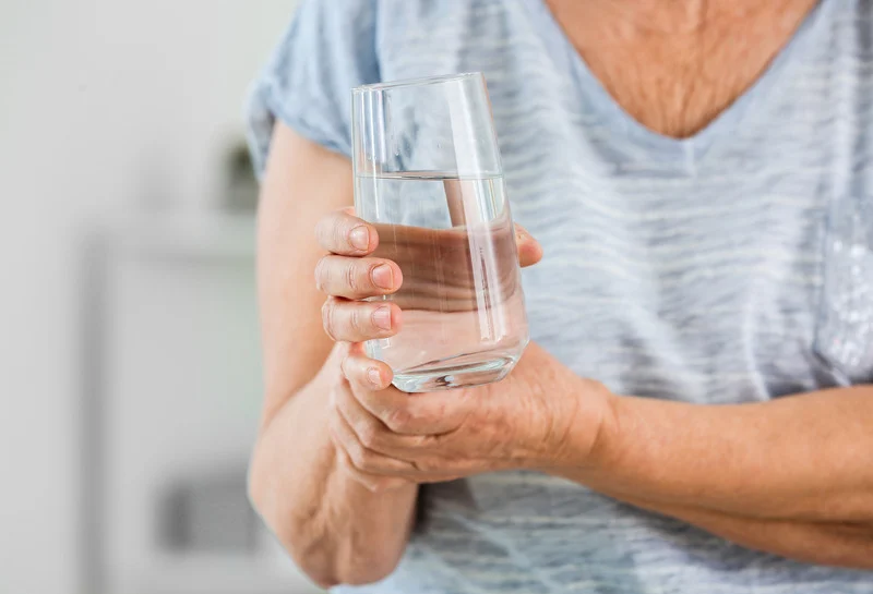 Parkinsonova bolest, žena pridržava rukom drugu ruku dok drži čašu
