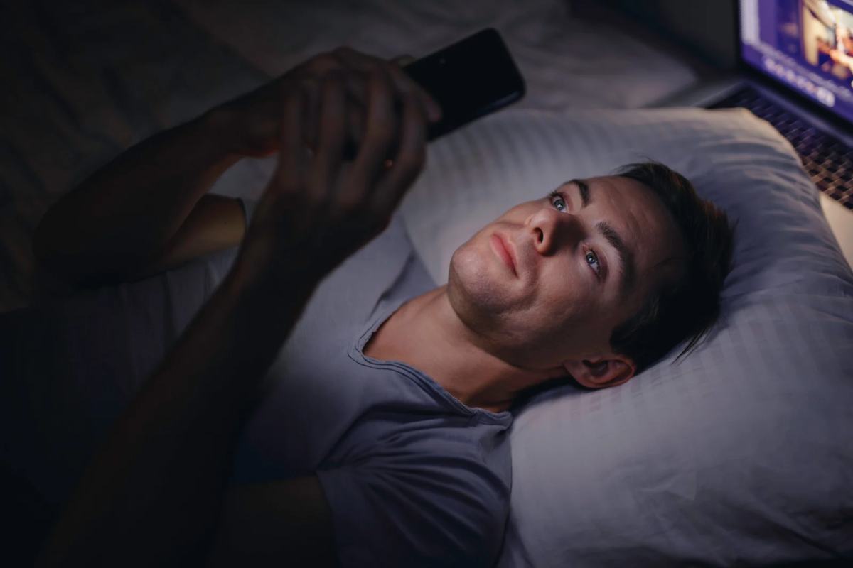 Muškarac scrola na mobitelu prije spavanja